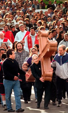 (RNS) Followed by more than 1,500 Good Friday worshippers in 2000, Jessie Rodriguez carries a cross that once stood atop Sacred Heart Church in Aurora, Ill. The scene is part of a ``Way of the Cross,'' or Via Crucis, procession that re-enacts and commemorates the march of 
Jesus to his crucifixion. Religion News Service file photo by Steven Buyansky/The Beacon News. 