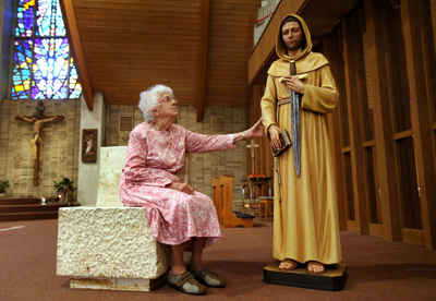 (RNS1-AUG27) Margaret Conetsco, 85, sits next to a wooden life-size statue of St. William inside the newly formed SS Robert & William Catholic Church in Euclid, Ohio.  Conetsco donated the statue after her former church, St. Robert, merged with  St. William. A statue of St. Robert was brought over, but St. William's never had a statue of St. William. For use with RNS-CHURCH-MERGE, transmitted Aug. 27, 2010. RNS photo by Marvin Fong / The Plain Dealer. 