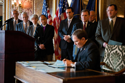 (RNS1-MAY12) Utah Gov. Gary Herbert signs a guest worker immigration bill into law as Mormon Bishop H. David Burton, second from left, looks on. The church's support of the law has upset many conservative Mormons, who view it as amnesty for illegal immigrants. For use with RNS-MORMONS-DIVIDE, transmitted May 12, 2011. RNS photo courtesy Church of Jesus Christ of Latter-day Saints. 