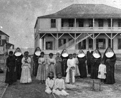 Gathered together in front of the Kapiolani Home for Girls are (left to right): Sr. M. Martha Kaiser, Sister M. Leopoldina Burns, Sr. Rosalia McLaughlin, Sr. M. Crescentia Eilers, Walter Murray Gibson, Mother Marianne Cope, and Sr. M. Charles Hoffmann. With them are the first ten girls sent to the Kapiolani Home from Kalaupapa, including the youngest -- Ana Iopa -- who can be seen to the far right. The Kapiolani Home was established on the grounds of the Kakaako Branch Hospital in Honolulu to care for daughters born to individuals at Kalaupapa. 