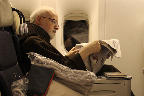 The Archbishop of Boston Cardinal Seán O'Malley, OFM, Cap. catches up on the news aboard a flight to Rome on Tuesday, February 26, 2013. Cardinal O’Malley will be joining his fellow cardinals for a meeting with the Holy Father, Pope Benedict XVI on Thursday, February 28, 2013.  RNS photo by Gregory L. Tracy, The Pilot.