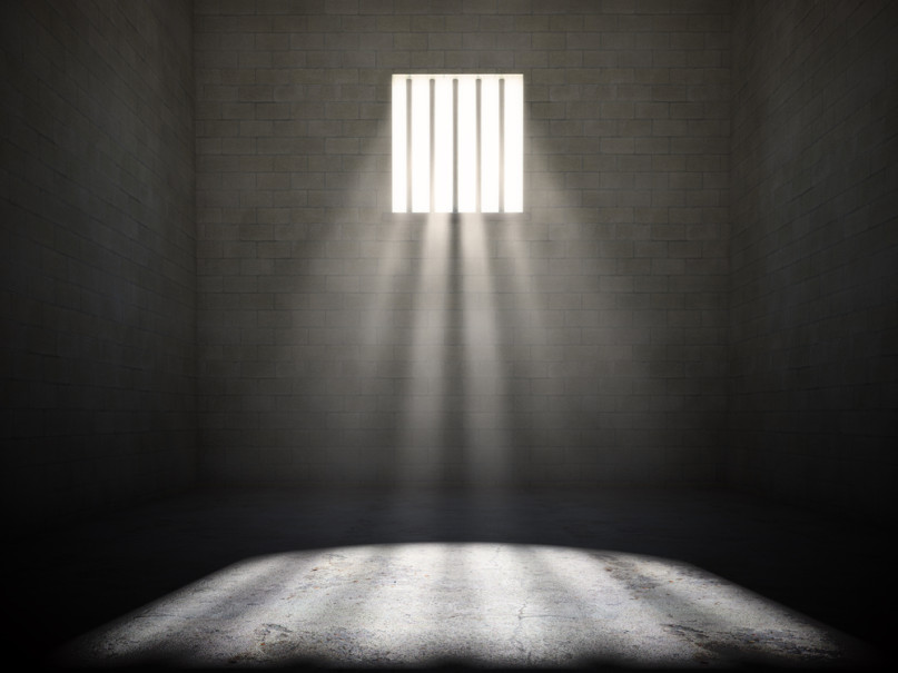 Interior of a prison cell with light shining through a barred window.  Photo courtesy Shutterstock (http://shutr.bz/104haw9)