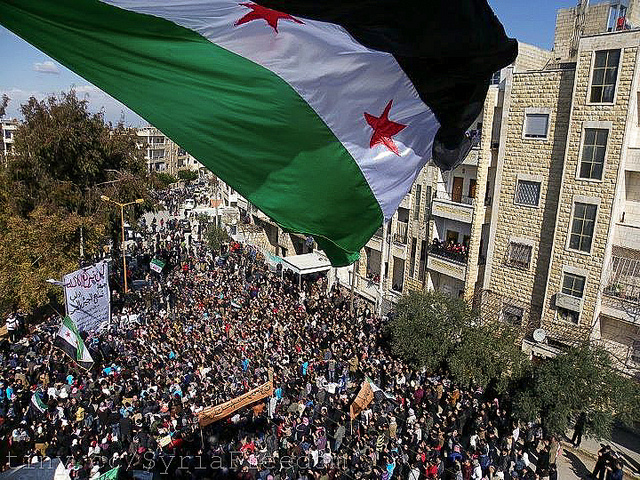 Syria independence flag flies over a large pathering of protesters in Idlib. Photo courtesy FreedomHouse via Flickr (http://flic.kr/p/bBd4br)