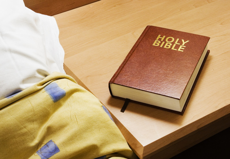 Photo of a Bible next to a bed, courtesy Shutterstock.
