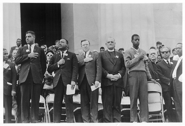 A young usher, holding cap at right, stands solemnly with religious, civil rights and labor leaders on the platform in front of the Lincoln Memorial during the national anthem at the opening of the March on Washington for Jobs and Freedom program on Aug. 28, 1963. Five of the 10 chairmen of the march also on the platform were, from left to right: Whitney M. Young Jr., executive director of the National Urban League; the Rev. Martin Luther King Jr., president of the Southern Christian Leadership Conference; Walter P. Reuther, president of the United Automobile Workers Union; the Rev. Eugene Carson Blake, chief executive officer of the United Presbyterian Church in the U.S.A., and acting chairman of the National Council of Churches' Commission on Religion and Race; and, second from right, Rabbi Joachim Prinz, president of the American Jewish Congress. Religion News Service file photo