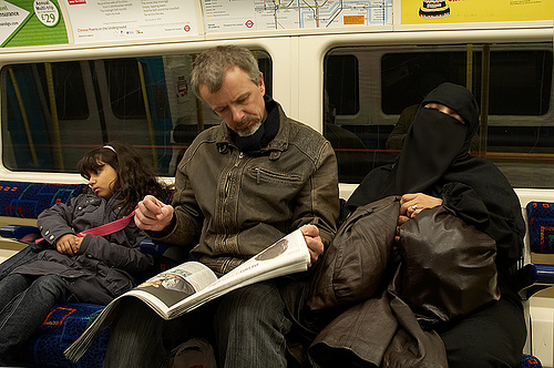 A woman wearing a niqab (far right) taps a nap in the London underground subway.