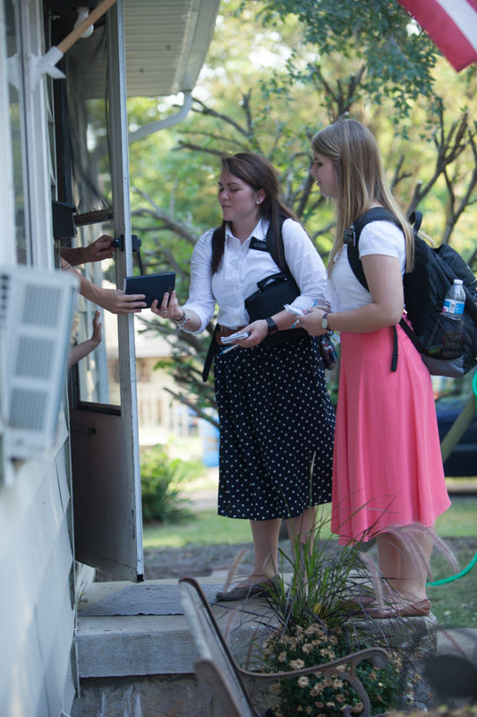 Sisters Ray (left) and Moody pass the Book of Mormon to a Kansas City, Mo., resident through her doorway while spreading their mission on Sept. 10, 2013. The sisters are carrying out their mission at the Church of Jesus Christ of Latter-day Saints' Independence Visitors' Center in Independence, Mo. RNS photo by Sally Morrow
