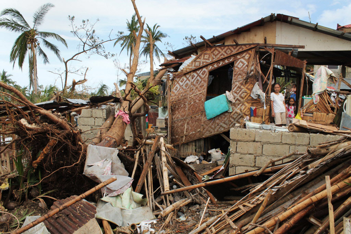 A family stands in front of their home battered by Typhoon Haiyan.  Photo by Pio Arce, courtesy of World Vision.
