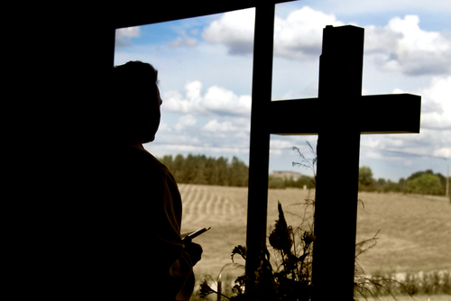 A clergy member next to a cross looking out a window.