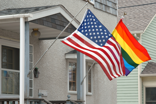 American and rainbow flag blowing in the wind on a suburban porch.
