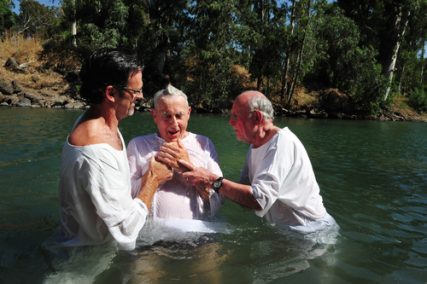 Two men prepare to dunk a third in a baptism rite in a river.