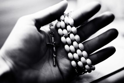 Photo of a hand holding a rosary with a cross.