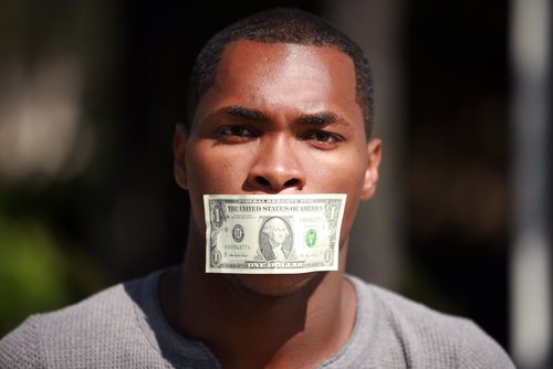 A young man wears a dollar bill taped over his mouth.