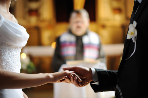 Bride and groom holding each other's hands during church wedding ceremony.