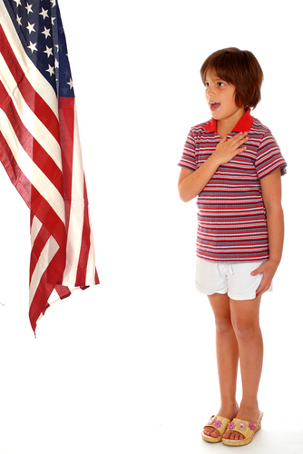 Elementary girl saying the Pledge of Allegiance toward a large American Flag. 