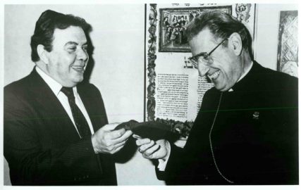 (1985) Then Archbishop John J. O'Connor, of the New York Roman Catholic Archdiocese, accepts a red yarmulke from Rabbi David B. Kahane of the Sutton Place Synagogue in New York City, prior to joining him on the bimah for a wide-ranging diologue in the synagogue's Jewish Town Hall series. Religion News Service file photo