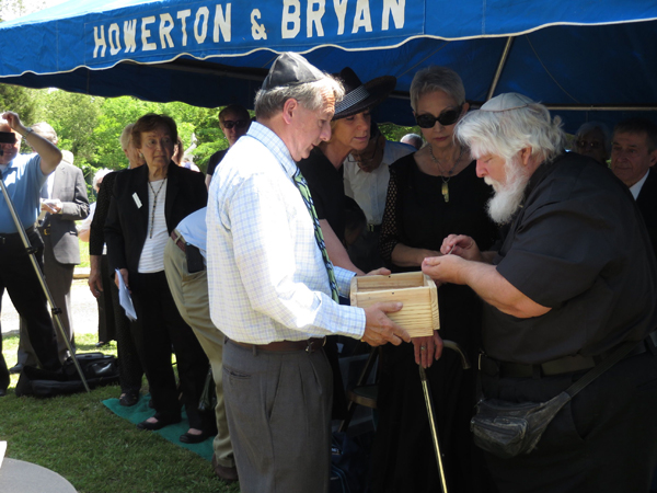 (RNS) David Klapper, left, of Beth El Synaoguge in Durham, N.C., holds a small burial box as Josphe Corbie deposits the ashes of Holocaust victims from the Dachau death camp in Germany. RNS photo by Yonat Shimron.
