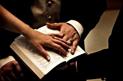 A bride and groom place their hands on a Bible during a wedding ceremony. Photo by Greg Kendall-Ball