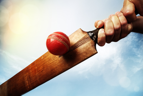 Cricket batsman hitting a ball shot from below against a blue sky.