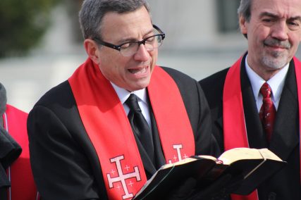 The Rev. Rob Schenck, founder of the Faith and Action ministry in Washington, D.C., reads from the Gospel of Luke during his ministry’s Live Nativity in front of the Supreme Court on Dec. 11, 2014. To his left is the Rev. Gary R. Ross of Midway Assembly of God in Lewes Del., whose members portrayed many of the characters in the event. Religion News Service photo by Adelle M. Banks