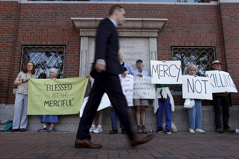 A pedestrian walks past death penalty protesters before the formal sentencing of convicted Boston Marathon bomber Dzhokhar Tsarnaev at the federal courthouse in Boston, Massachusetts on June 24, 2015. Photo courtesy of REUTERS/Dominick Reuter