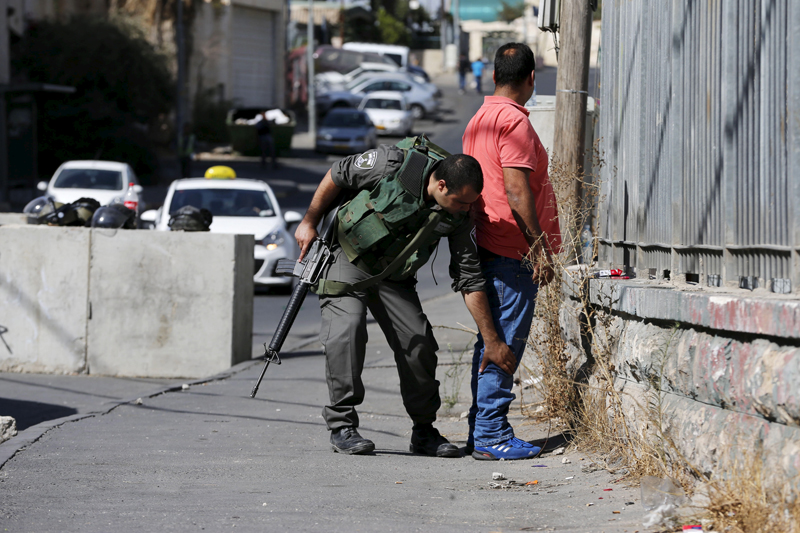 An Israeli border policeman checks a Palestinian man at a new roadblock in East Jerusalem on October 15, 2015. Israel set up roadblocks in Palestinian neighbourhoods in East Jerusalem and deployed soldiers across the country on Wednesday in an effort to stop a wave of Palestinian knife attacks. Photo courtesy of REUTERS/Ammar Awad