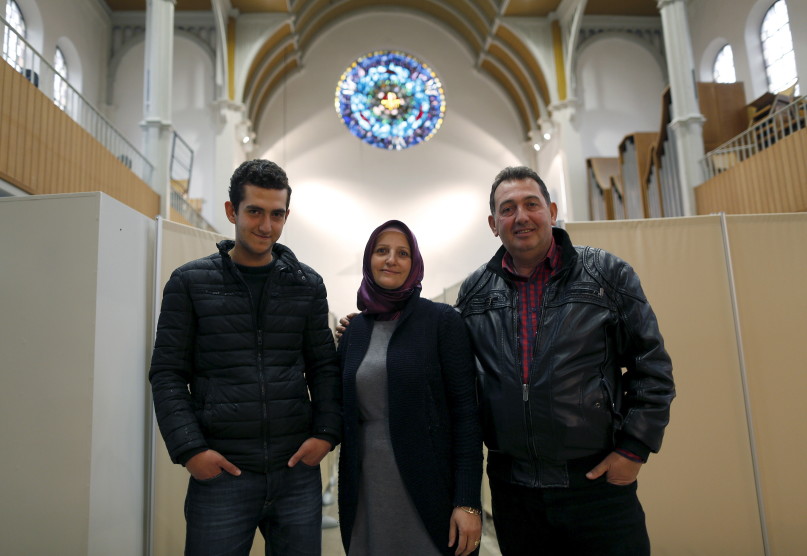 Members of a migrant Syrian family, Zabyl Olabi (C), her husband Mahmod and their 18-year-old son Humam (L), who came from Haleb near Aleppo, pose inside a Protestant church in Oberhausen, Germany November 19, 2015. Up to 140 refugees are landing in Oberhausen every week, forcing authorities to come up with new locations to house them. City officials say they had little choice but to use the church. In early November, workers removed the altar and dozens of chairs, replacing them with metal beds, which are separated by makeshift partitions to give the church's new residents a semblance of privacy. Picture taken November 19, 2015. To match story EUROPE-MIGRANTS/GERMANY-CHURCH     REUTERS/Ina Fassbender - RTX1VX13