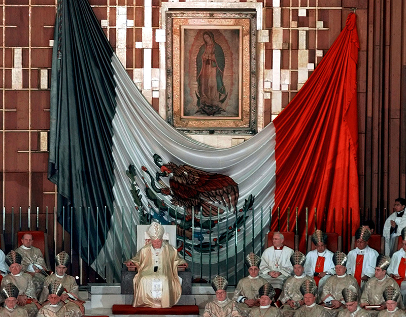 Pope John Paul II sits under the Lady of Guadalupe and the Mexican national flag during a mass at the Basilica of Our Lady of Guadalupe in Mexico City, on January 23, 1999. Photo courtesy of REUTERS *Editors: This photo may only be republished with RNS-POPE-BORDER, originally transmitted on Nov. 4, 2015.