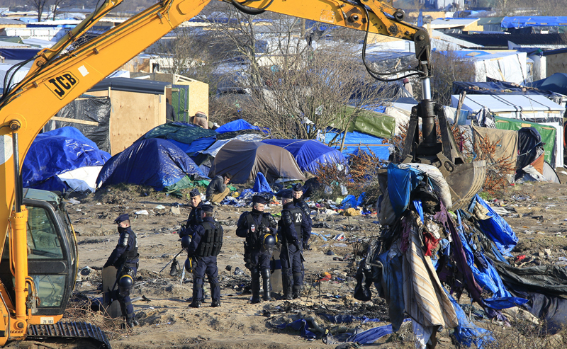 French police officers secure the area as a crane is used to clear dismantled shelters of the camp known as the 