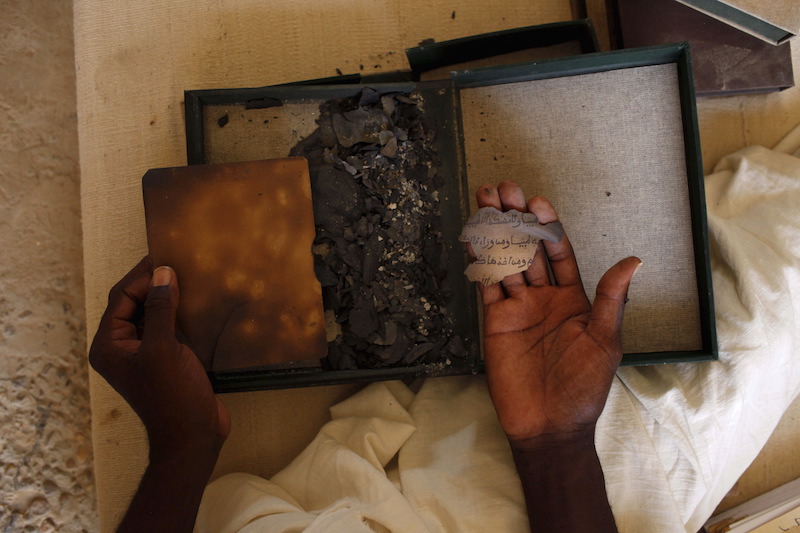 Alkanis Cisse holds the remnants of an ancient Islamic manuscript burned by Islamist militants at the Ahmed Baba Centre for Islamic learning in Timbuktu, Mali, July 25, 2013. A former trainee teacher accused of damaging monuments in the name of Islam in the ancient Malian city of Timbuktu will stand before the International Criminal Court on March 1, 2016 for a hearing to decide if he should face a landmark trial. Picture taken July 25, 2013. REUTERS/Joe Penney.