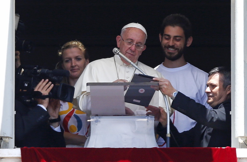 Pope Francis is flanked by two Polish youths as he uses an iPad to make the first online registration for the next 2016 World Youth Day in Poland, as he leads the Angelus prayer from the window of the Apostolic palace in Saint Peter's Square at the Vatican July 26, 2015. Photo courtesy REUTERS/Max Rossi 