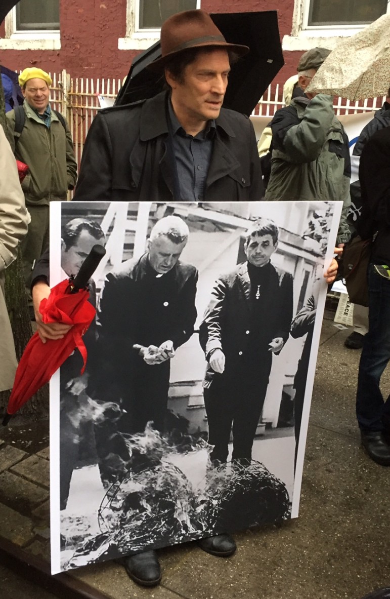 Mourner carries a photo of Frs Phil and Dan Berrigan burning draft records during '68 protest of Vietnam War