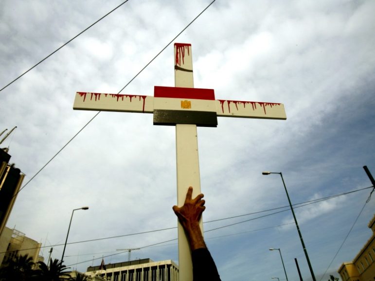An Egyptian Coptic Christian holds a cross with the Egyptian flag during a demonstration outside the Egyptian embassy in Athens April 19, 2006. Hundreds of Egyptians living in Greece marched through Athens to protest against sectarian tension following a series of attacks on Coptic Christian church-goers in Alexandria, Egypt, with activists blaming the government for failing to subdue rising inter-denominational friction. Photo courtesy of Yannis Behrakis/Reuters