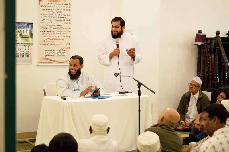 Imam Jawad Rasul at the microphone making an introduction for visiting Imam Shadeed Muhammad, seated. Photo courtesy Hassan Younas