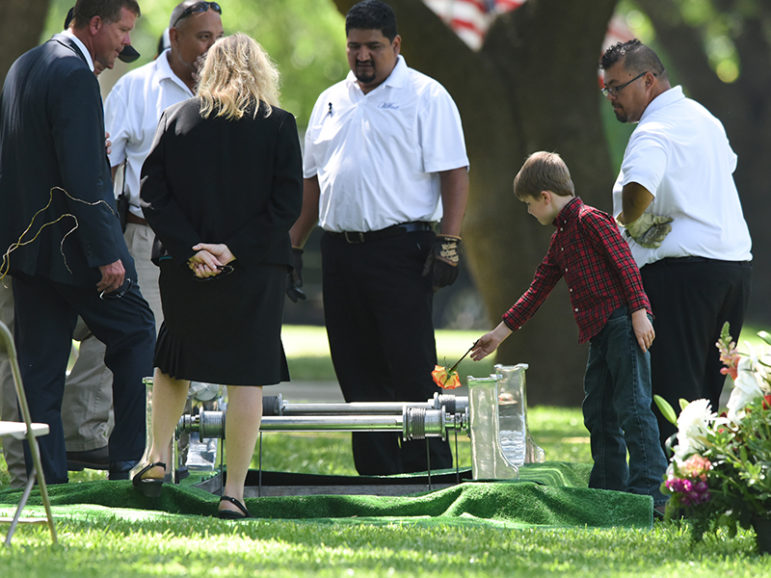 Magnus Ahrens drops a flower into the grave of his father, Dallas Police Department Senior Corporal Lorne B. Ahrens, who was among five police officers shot dead the previous week, after the burial ceremony at Restland Public Safety Memorial Gardens in Dallas on  July 13, 2016. Photo courtesy of REUTERS/Cooper Neill