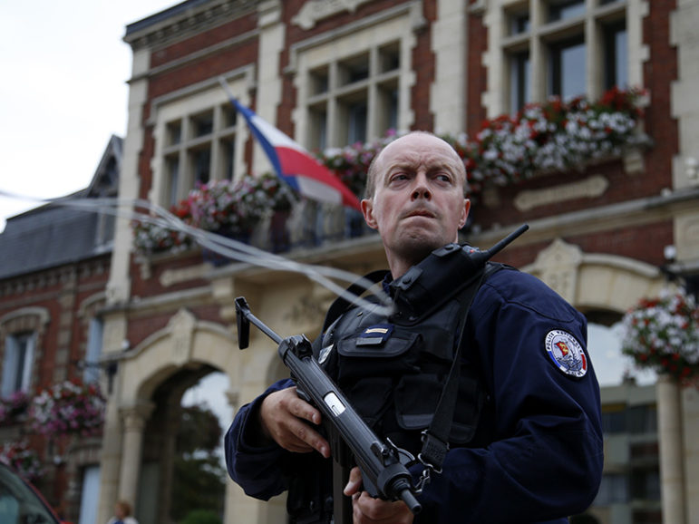 A policeman secures a position in front of the city hall after two assailants took five people hostage in the church at Saint-Etienne-du-Rouvray near Rouen in Normandy, France, July 26, 2016. The attackers killed a priest and seriously wounded another hostage before being shot dead by police. Courtesy of REUTERS/Pascal Rossignol