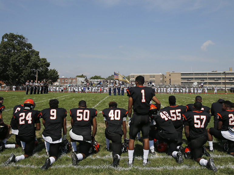 Woodrow Wilson High's Edwin Lopez (#1) stands while most of his teammates and coaches kneel during the national anthem before their game against Highland High School on Sept. 10, 2016, in Camden, N.J. Photo courtesy of Yong Kim/Philly.com
