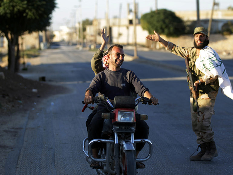 Residents driving a motorcycle gesture towards a fighter in Dabiq town, northern Aleppo countryside, Syria October 16, 2016. Courtesy of REUTERS/Khalil Ashawi