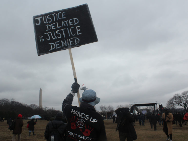 David Barrows of Washington, D.C., carries a “Justice Delayed Is Justice Denied” sign with the Washington Monument in the background. Civil rights leader Al Sharpton organized the 