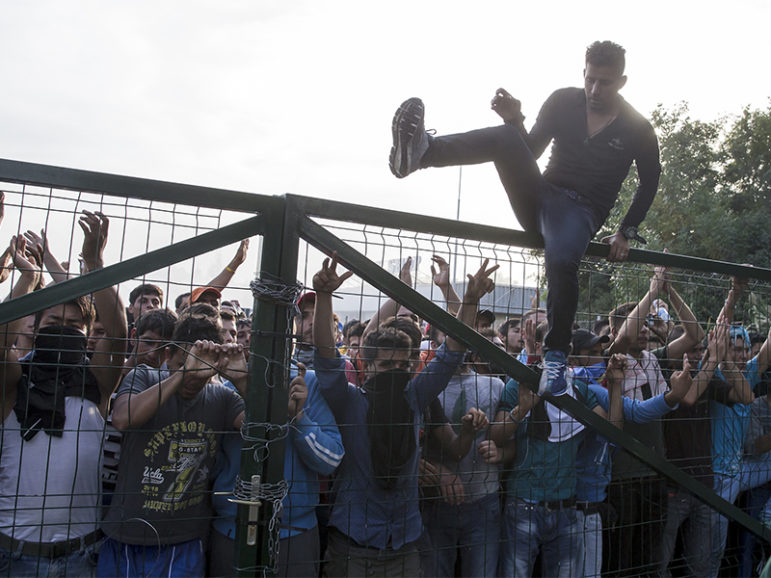 A migrant climbs a fence during clashes with Hungarian riot police at the border crossing with Serbia in Roszke, Hungary, on Sept. 16, 2015. Hungarian police fired tear gas and water cannon at protesting migrants who were demanding they be allowed to enter from Serbia. Photo courtesy of Reuters/Marko Djurica