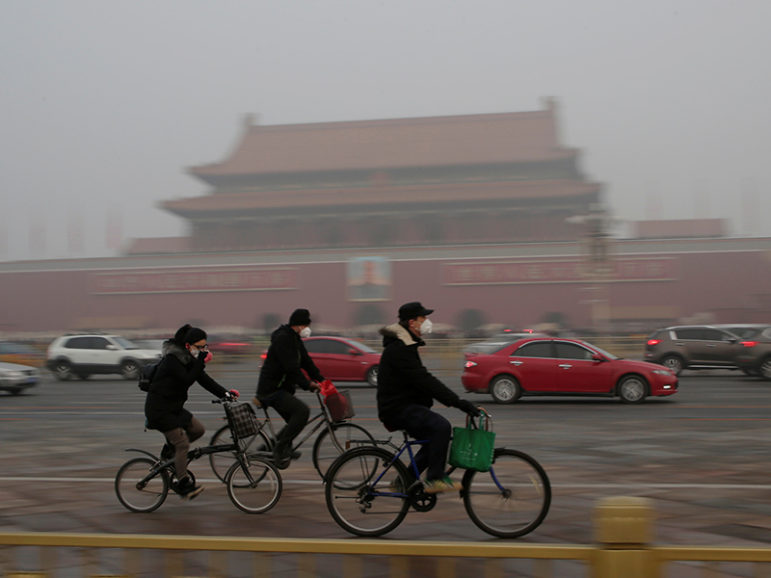 People wearing masks cycle past Tiananmen Gate through smog after a red alert was issued for heavy air pollution in Beijing on Dec. 20, 2016. Photo courtesy of Reuters/Jason Lee