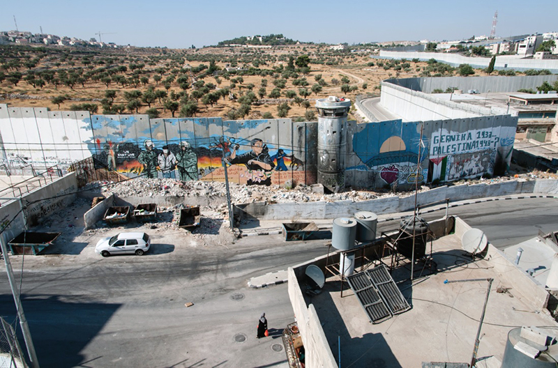 The Israeli separation wall divides Aida Refugee Camp from adjacent olive groves on land belonging to the West Bank town of Bethlehem on June 15, 2016. The Israeli settlement of Gilo continues to expand on a nearby hillside.Photo courtesy of Creative Commons/Palestine Israel Ecumenical Forum