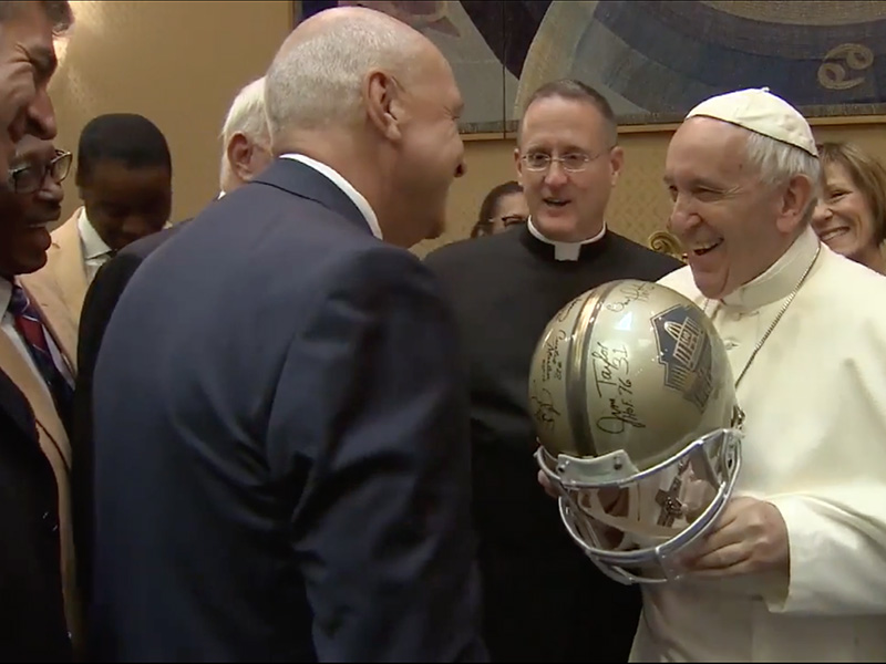Pope Francis jokes with an NFL Hall of Fame representative about wearing a helmet that was a gift for the pope during a visit at the Vatican on June 21, 2017. Screenshot from video