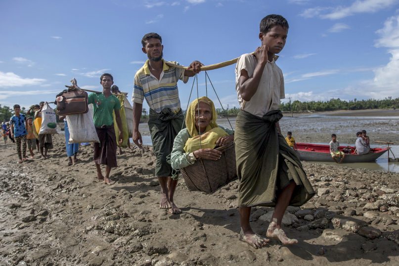 Rohingya Muslims, who crossed over from Myanmar into Bangladesh, carry an elderly woman in a basket and walk toward a refugee camp in Shah Porir Dwip, Bangladesh, on Sept. 14, 2017. (AP Photo/Dar Yasin)