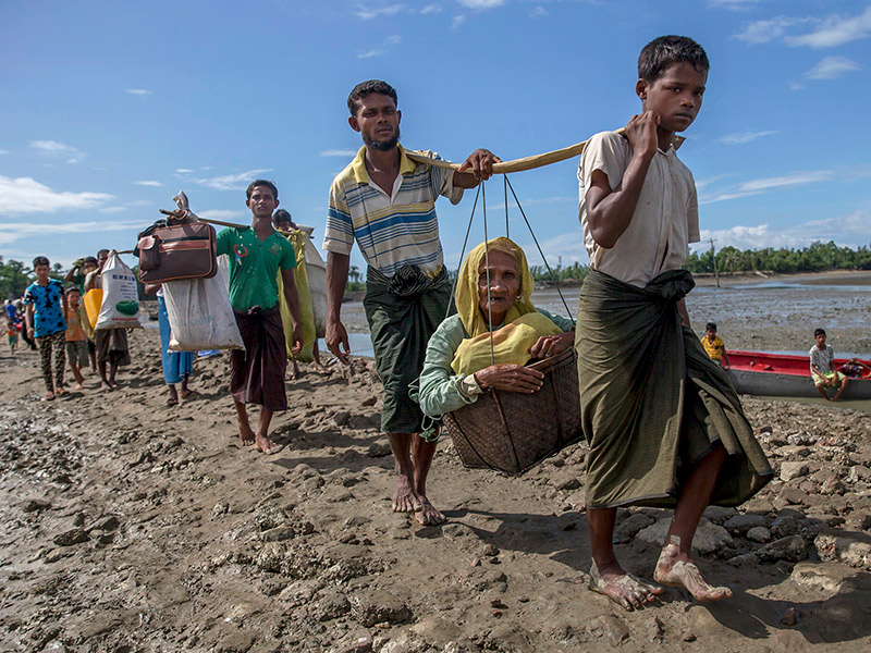 Rohingya Muslims, who crossed over from Myanmar into Bangladesh, carry an elderly woman in a basket and walk toward a refugee camp in Shah Porir Dwip, Bangladesh, on Sept. 14, 2017. AP Photo/Dar Yasin