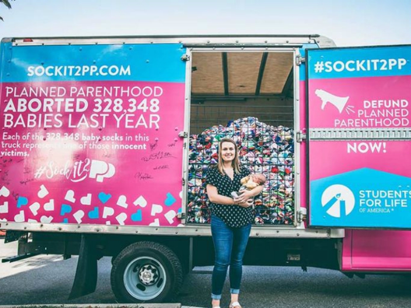 Maddi Runkles and her baby boy Greyson pose for a portrait in front of a truck sponsored by Students for Life of America and filled with 328,348 baby socks. Photo courtesy of Students for Life of America