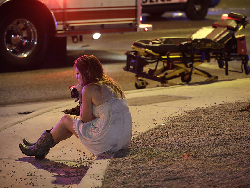 A woman sits on a curb at the scene of a shooting outside of a music festival along the Las Vegas Strip, Monday, Oct. 2, 2017, in Las Vegas. Multiple victims were being transported to hospitals after a shooting late Sunday at a music festival on the Las Vegas Strip. (AP Photo/John Locher)