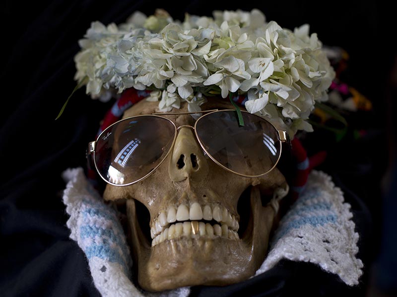 A human skull wearing sun glasses and flowers is displayed outside the General Cemetery chapel during the Natitas Festival in La Paz, Bolivia, Wednesday, Nov. 8, 2017. Every year, hundreds of Bolivians carry human skulls adorned with flowers to a cemetery in La Paz, asking for money, health, and other favors as part of a festival. (AP Photo/Juan Karita)