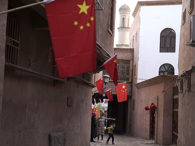 In this Nov. 4, 2017, photo, a child reacts to a stranger as adults chat along the corridor of the old city district where Chinese national flags are prominently hung in Kashgar in western China's Xinjiang region. Authorities are using detentions in political indoctrination centers and data-driven surveillance to impose a digital police state in the region of Xinjiang and its Uighurs, a 10-million strong, Turkic-speaking Muslim minority Beijing fears could be influenced by extremism. (AP Photo/Ng Han Guan)