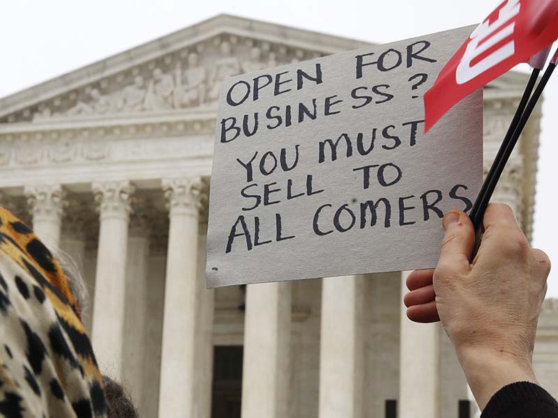 A woman holds up a sign as people gather outside of the Supreme Court while it hears arguments in the Masterpiece Cakeshop v. Colorado Civil Rights Commission case on Dec. 5, 2017, in Washington. (AP Photo/Jacquelyn Martin)